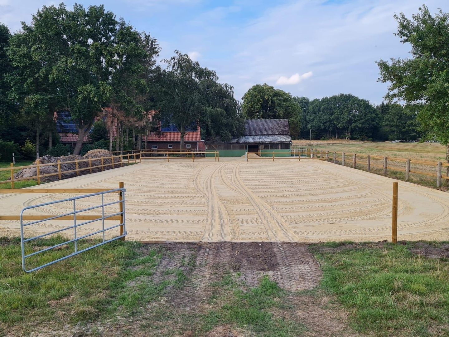 Ein neu gestalteter Reitplatz mit Sandboden und Umzäunung.